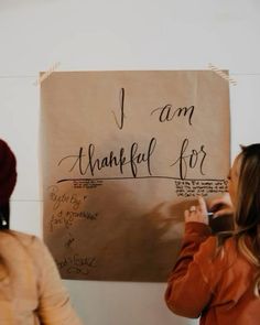 two women standing in front of a sign that says i am grateful for