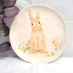 a plate with a drawing of a rabbit on it next to purple flowers and leaves