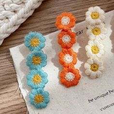 three crocheted flower clips sitting on top of a piece of paper next to yarn