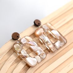 Simple, minimal, super shiny, and smooth, these open square earrings go with everything! Just look at the shimmer of the mother-of-pearl shells hanging on the contrasting wood stud posts. They're lightweight, hang beautifully, and are a perfect gift or accessory for friends and shell lovers of all ages. These are a classic collection to keep or gift and share. Perfect for mothers, daughters, teens, hers/hers, bridesmaids, and BFF's. The pieces shown in the pictures demonstrate the style, size, shape, and color of the pendant you are buying. There may be slight variations in the appearance of the pendant you receive as each piece is lovingly handmade. DETAILS:  - Unique 100% handmade open square-shaped earrings made of resin and mother-of-pearl shells with wood stud posts - Each piece is ca Boho Mother, Wood Stud Earrings, Wood Earrings Stud, Wood Studs, Square Earrings, Shell Earrings, Classic Collection, Natural Pearls, For Friends