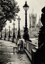 a black and white photo of a person sitting on a bench in front of the big ben clock tower