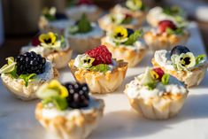 small cupcakes with fruit and cream toppings on a white tablecloth covered tray