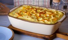 a casserole dish with potatoes and cheese on a wooden serving board next to plates