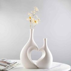 two white vases sitting on top of a table with flowers in the shape of a heart