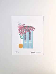 a card with a blue door and pink flowers on the outside, in front of a white wall