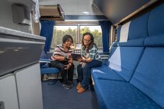 two people sitting in the back of a bus looking at something on a tablet computer