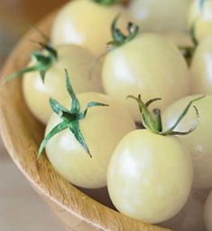 a wooden bowl filled with lots of white tomatoes