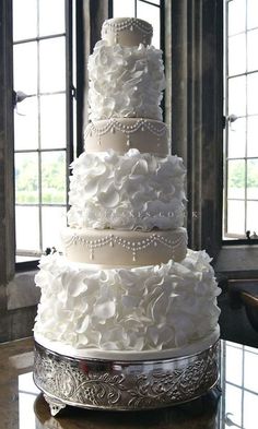 a white wedding cake sitting on top of a table next to a window with lots of windows