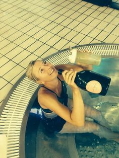 a woman sitting in a bathtub talking on a cell phone and drinking from a bottle