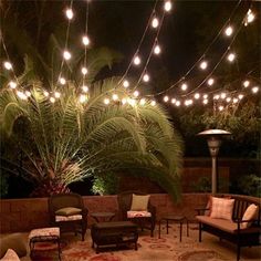 an outdoor seating area is lit up with string lights and pillows on the rugs