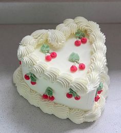 a heart shaped cake with white frosting and cherries on the top, sitting on a counter