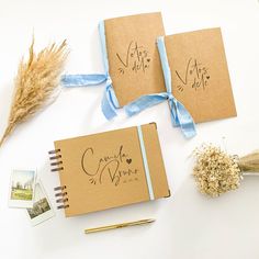 two brown notebooks with writing on them next to dried flowers and an ink pen