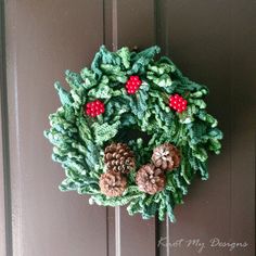 a crocheted wreath with pine cones and berries hanging on the front door handle