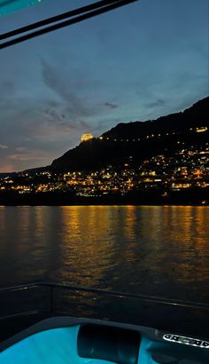 the city lights are lit up at night on the water's edge as seen from a boat