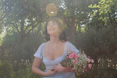 a woman in a blue dress holding a bouquet of flowers and looking up into the sky