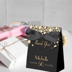 a black and gold thank you gift bag next to a white box with a pink bow