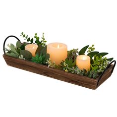 three lit candles sit in a wooden tray filled with greenery