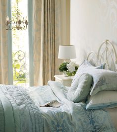 a bed with blue and white comforters in a bedroom next to a window filled with curtains