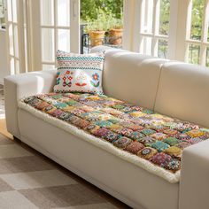 a white couch sitting in front of two windows with pillows on it's back