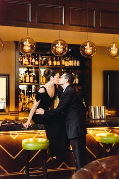 a man and woman kissing in front of a bar with lights hanging from the ceiling