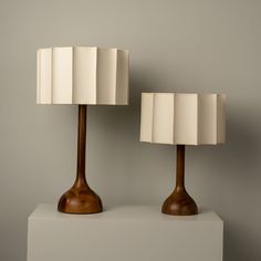 two wooden lamps sitting on top of a white shelf next to each other in front of a gray wall