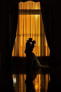 a bride and groom standing in front of a window at their wedding reception, silhouetted against the curtains