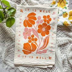 an orange and pink flower print on a white napkin next to some green leafy plants