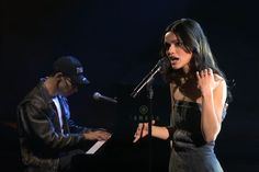 a woman standing in front of a microphone next to a man playing the piano on stage