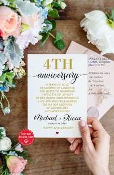 someone holding up a wedding anniversary card on top of a wooden table next to flowers