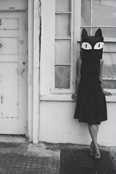 a woman standing in front of a door with a cat mask on