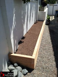 a wooden planter box sitting next to a white brick wall and some rocks on the ground