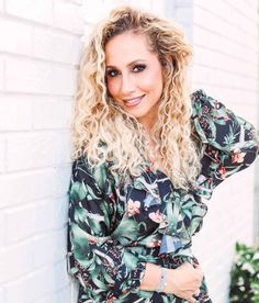 a woman leaning against a brick wall with her hands on her hips and smiling at the camera