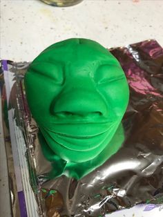 a close up of a green cake on tin foil with a face drawn on it