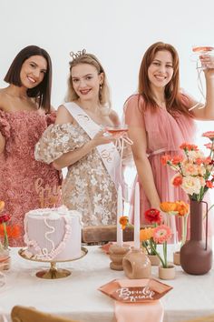 three beautiful women standing next to each other in front of a table with cake and flowers