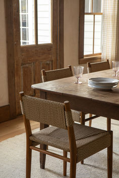 a wooden table with two chairs and plates on it in front of a doorway that leads to another room