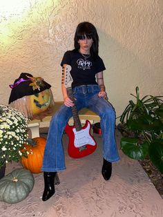 a woman sitting on a bench with a guitar in her lap and pumpkins behind her