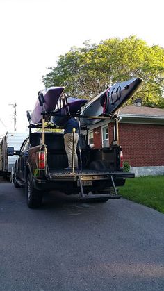 the back of a truck with kayaks on it's flatbed is parked in front of a house