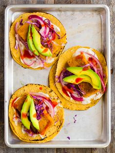 three tortillas topped with avocado and red cabbage on a baking sheet