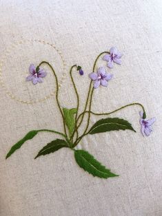 some purple flowers are embroidered onto a white linen pillow with green leaves and beading