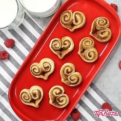 some cinnamon rolls are on a red tray with raspberries next to it and a glass of milk