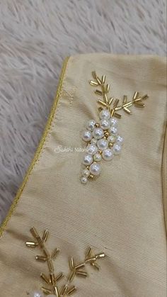 an embroidered piece with pearls and gold leaves on it, sitting on a white furnishing