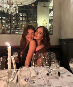 two women are sitting at a table with wine glasses and candles in front of them