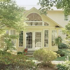 a yellow house with white trim and windows on the front door is surrounded by greenery