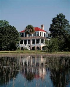 a large white house sitting on top of a lush green field next to a lake