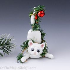 a white cat sitting on top of a christmas tree next to a potted plant