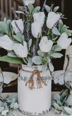 a white vase with flowers and greenery on a table