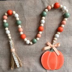 an orange and white beaded necklace next to a pumpkin shaped pendant on a gray cloth