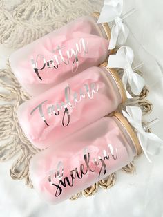 three pink personalized water bottles sitting on top of a white bed with ribbons around them