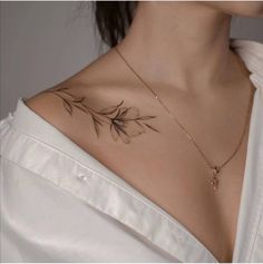 a woman with a tattoo on her chest is wearing a white shirt and gold necklace