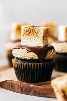 cupcakes with chocolate frosting and marshmallows are on a cutting board